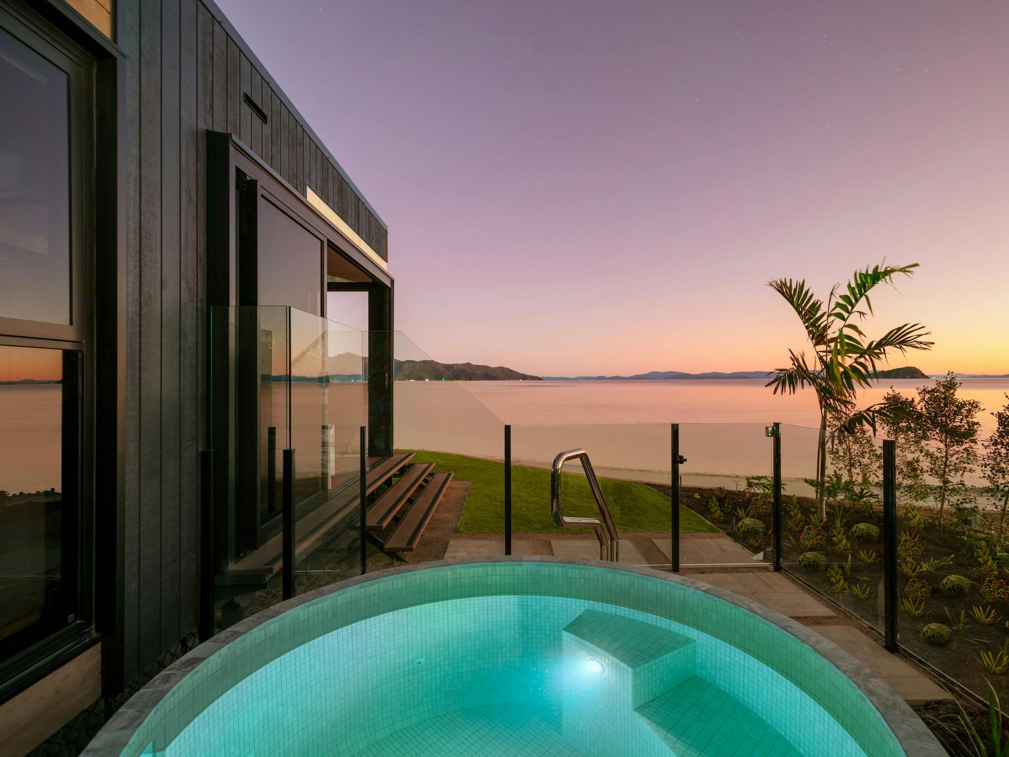 A glowing private pool with steps, overlooking a serene ocean view at sunset, surrounded by greenery A glowing private pool with steps, overlooking a serene ocean view at sunset, surrounded by greenery