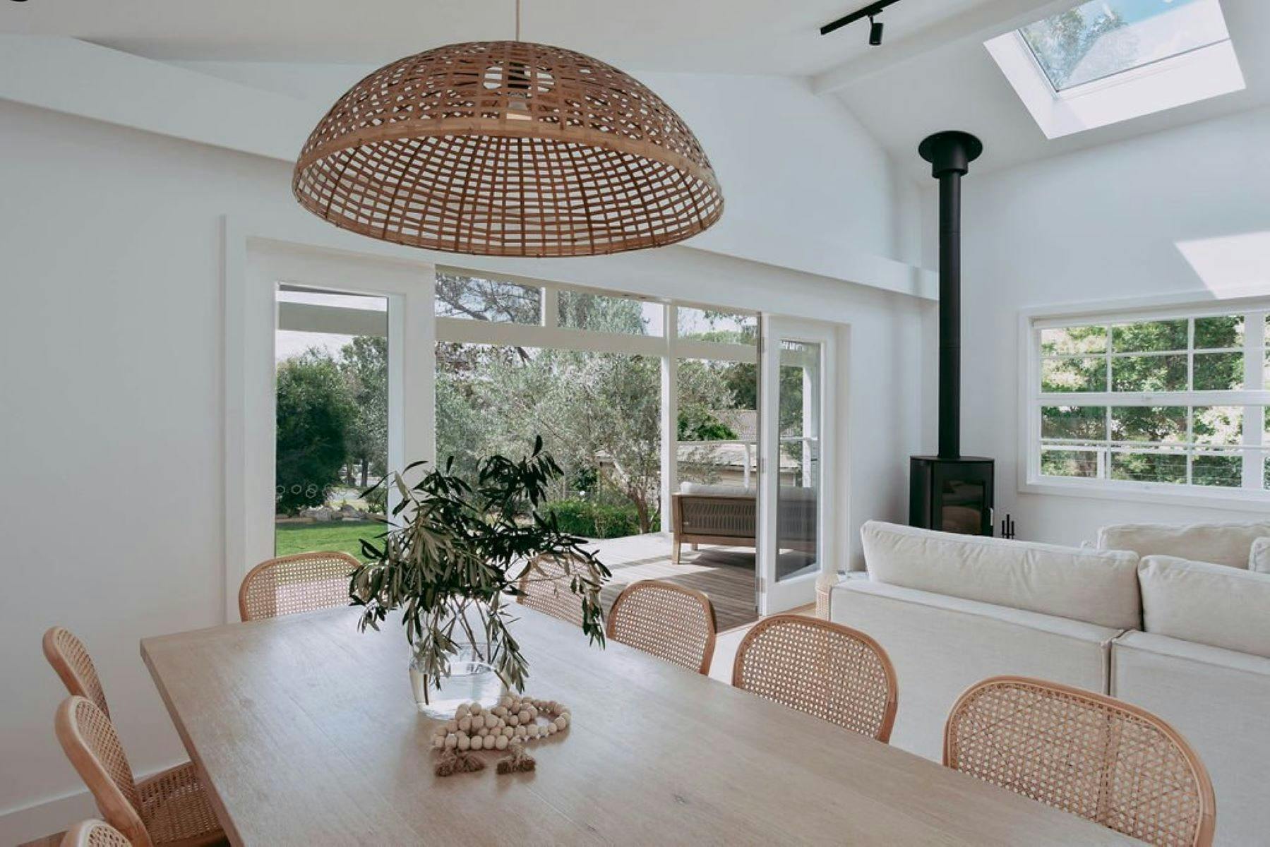 Image is on dining area. Large rattan pendant hangs above dining table. Fireplace in back ground