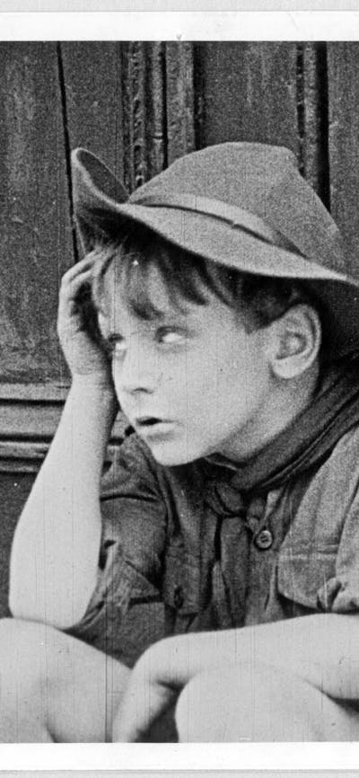 Black and white film still of young boy wearing hat rolling his eyes
