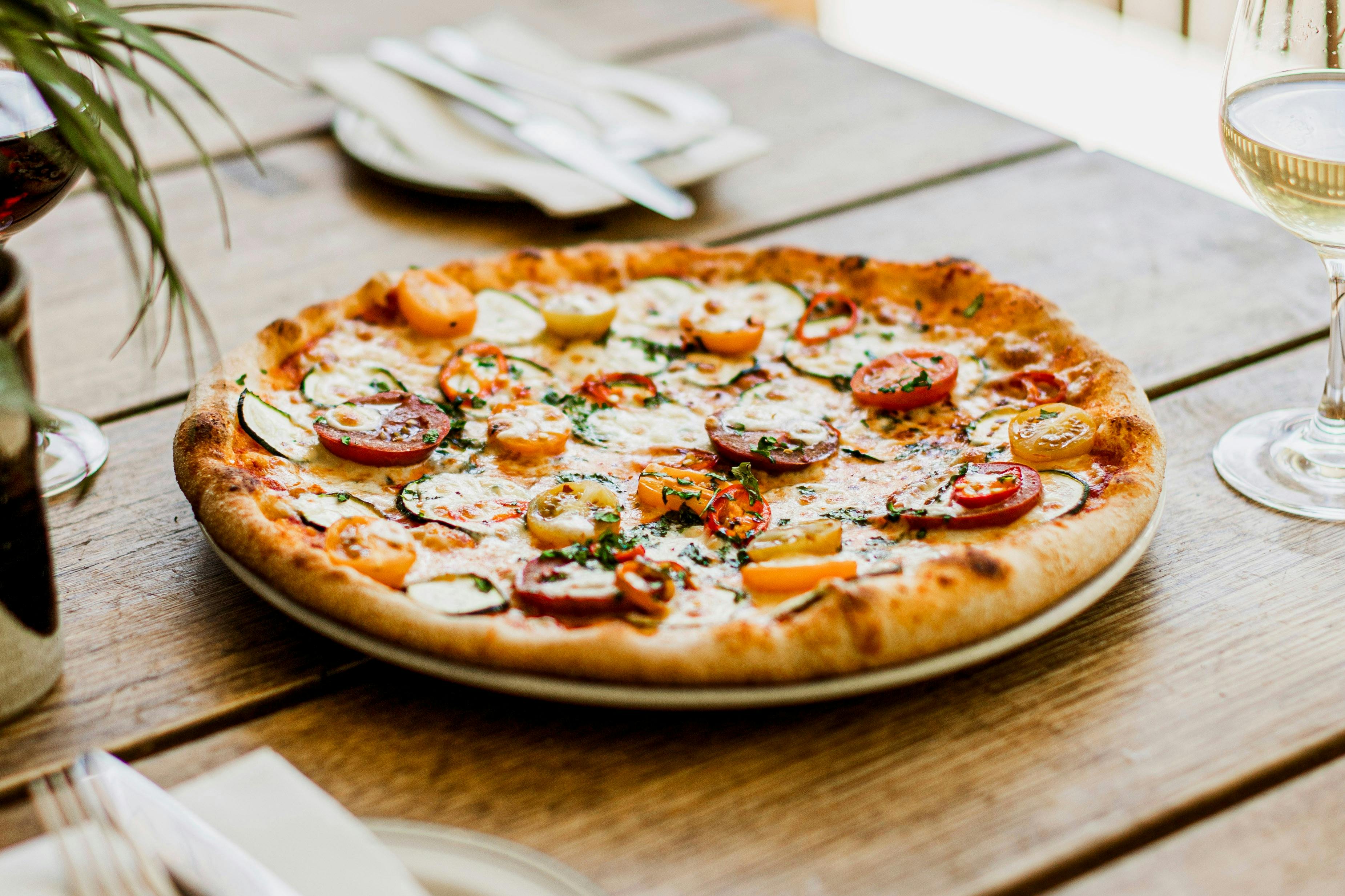 Tomato and zucchini pizza on plate and glass of white wine, on wooden picnic table