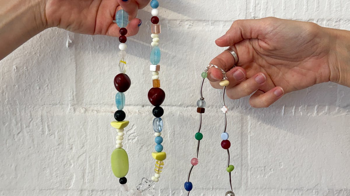 Two hands holding colourful beaded necklaces