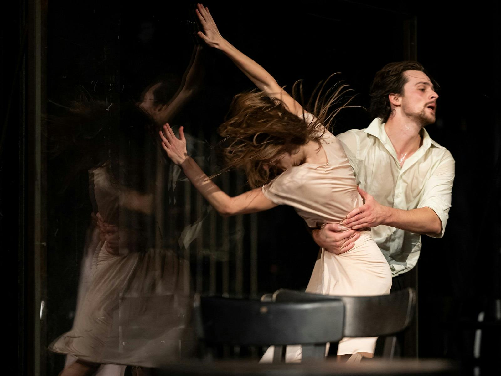 Two dancers in motion. One has a beard and is holding the other around the waist.