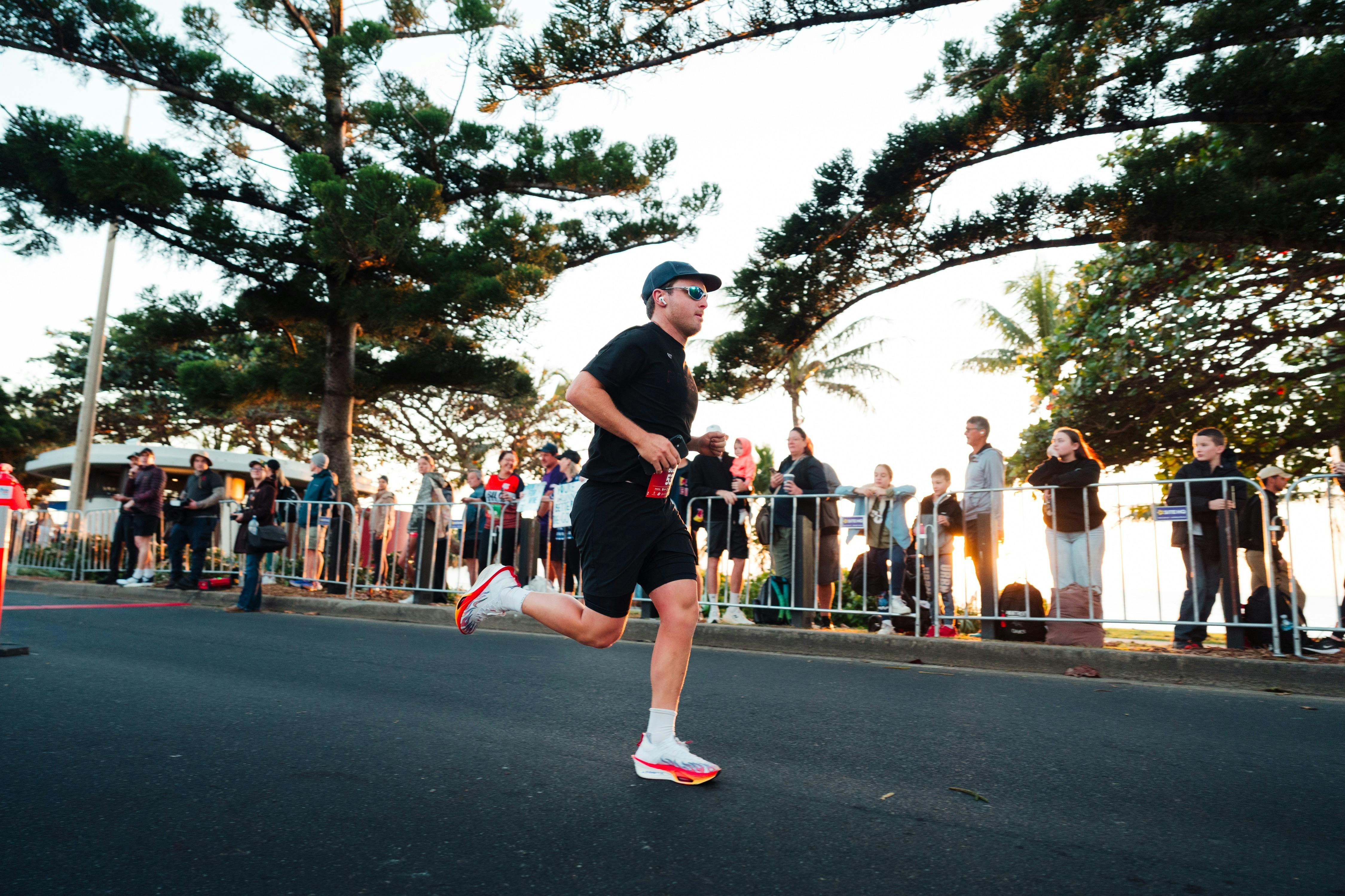 Runners make their way along a coastal road overlooking the water and surrounding Yeppoon hills.