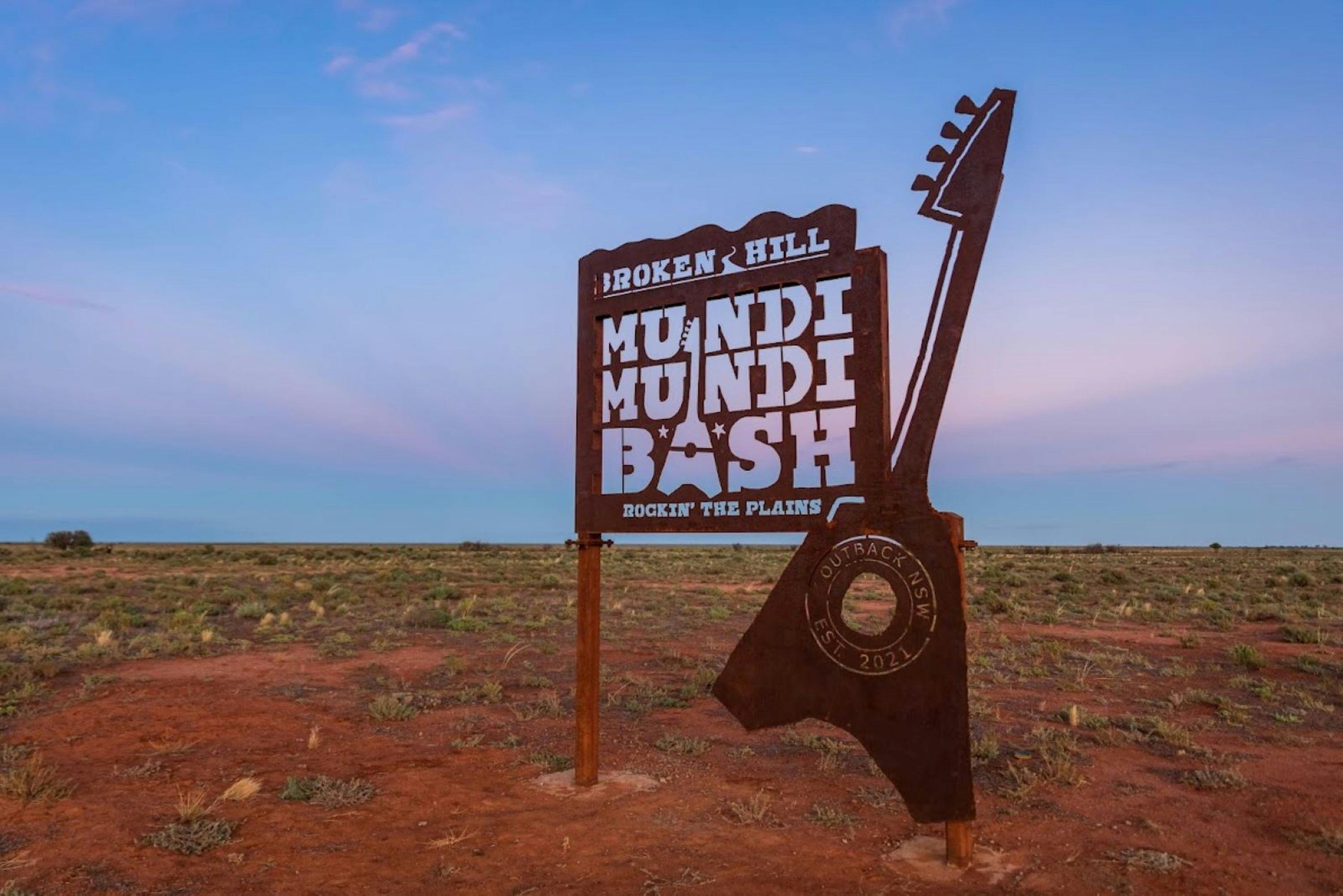 The sign for the Broken Hill Mundi Mundi Bash with a guitar sits infront of the Mundi Mundi Plains