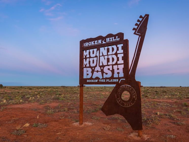 The sign for the Broken Hill Mundi Mundi Bash with a guitar sits infront of the Mundi Mundi Plains