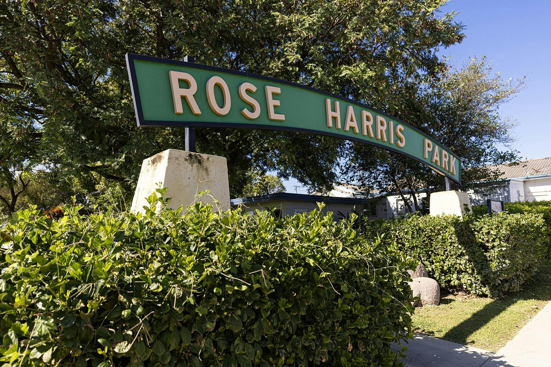 Green entrance sign to Rose Hill Park, with gardens around and footpaths.