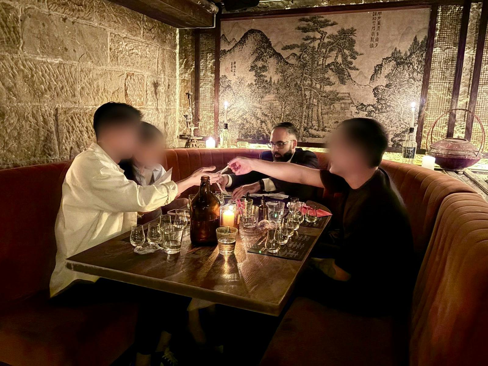 Guests reach across a candlelit table in a velvet booth as Magic Manny performs, with sandstone wall