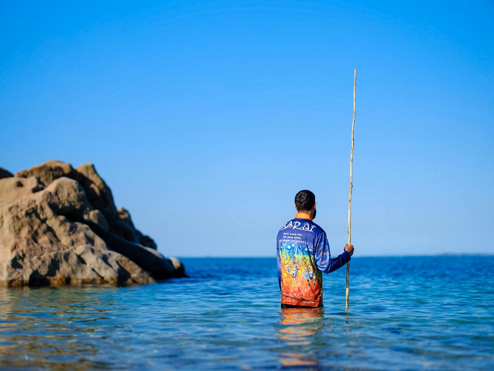 Man standing in water fishing with spear.