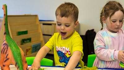 A young boy wearing a yellow shirt with blue dinosaur plays with toy dinosaurs at Science Time