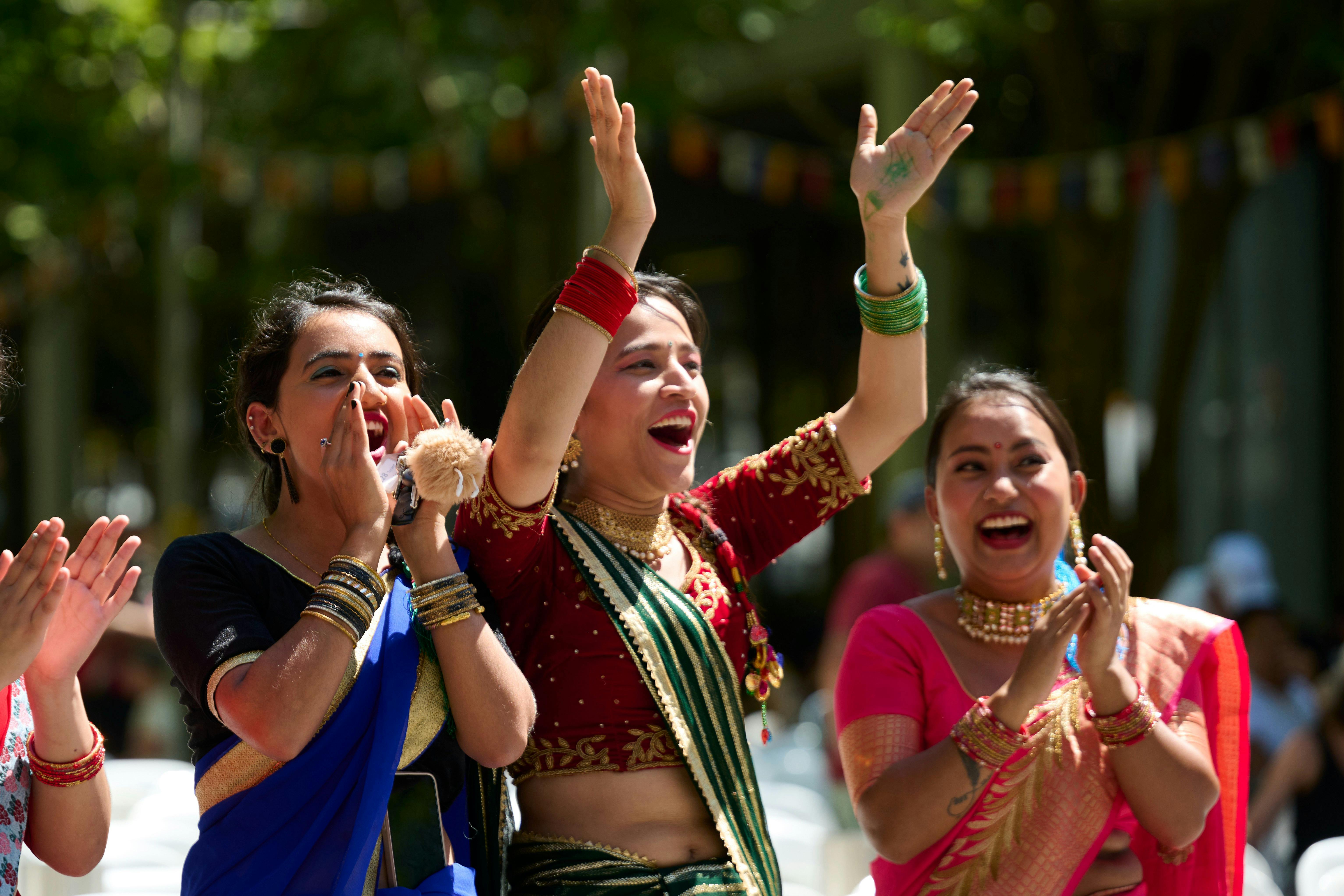 Three women in cultural dress clap for the festival parade performers