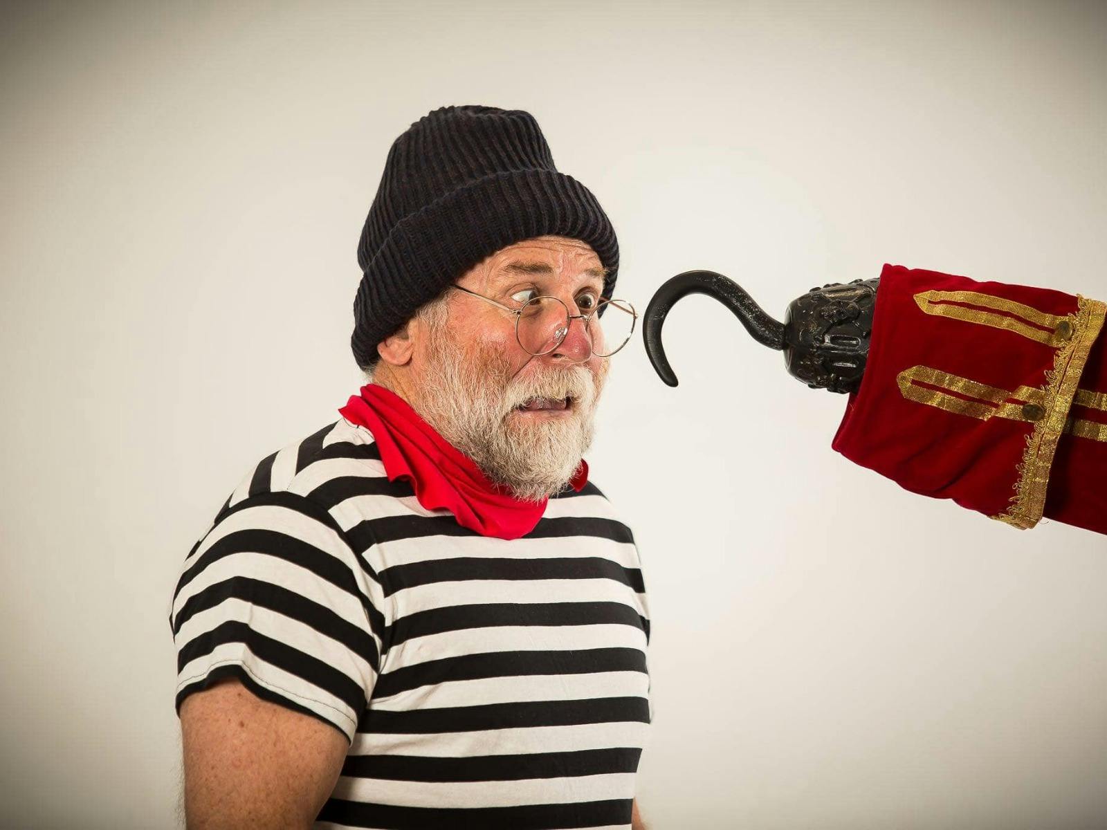 An older man with a white beard and round glasses looks surprised, wearing striped shirt and beanie