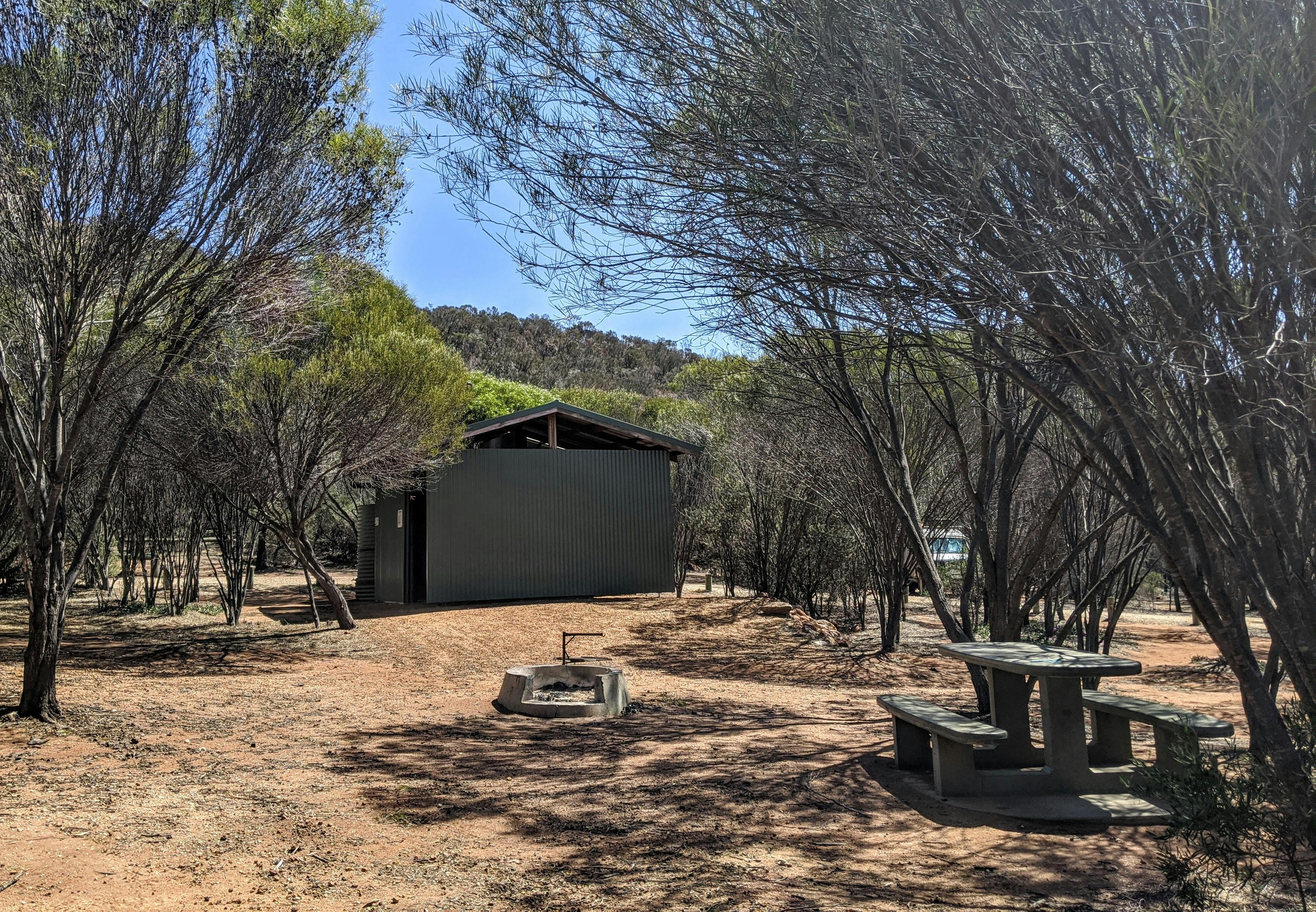 Concrete fire ring, picnic table and bench and building.
