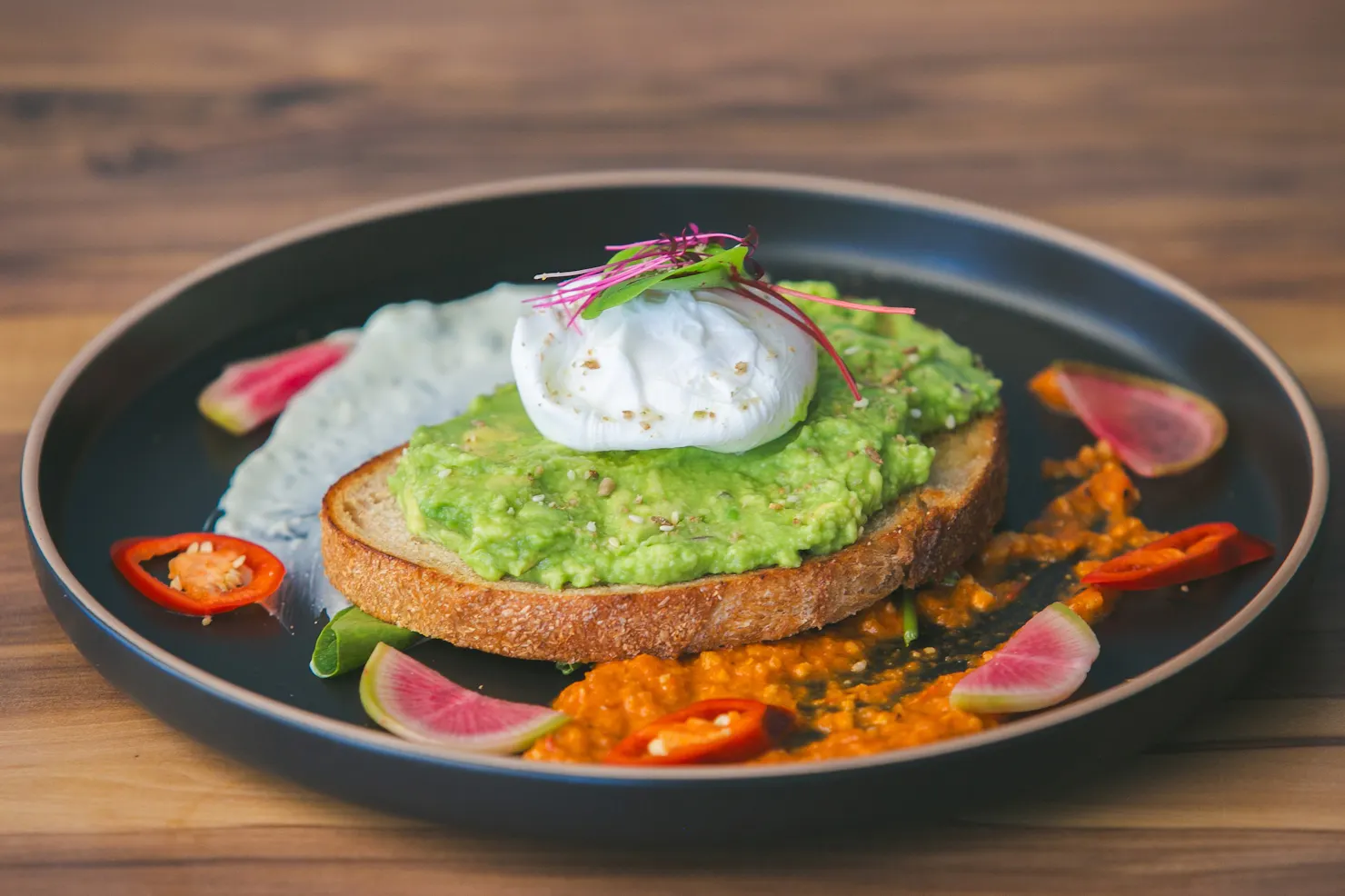 Smashed avocado on toasted sourdough with whipped feta, a poached egg and dukkah on a dark plate