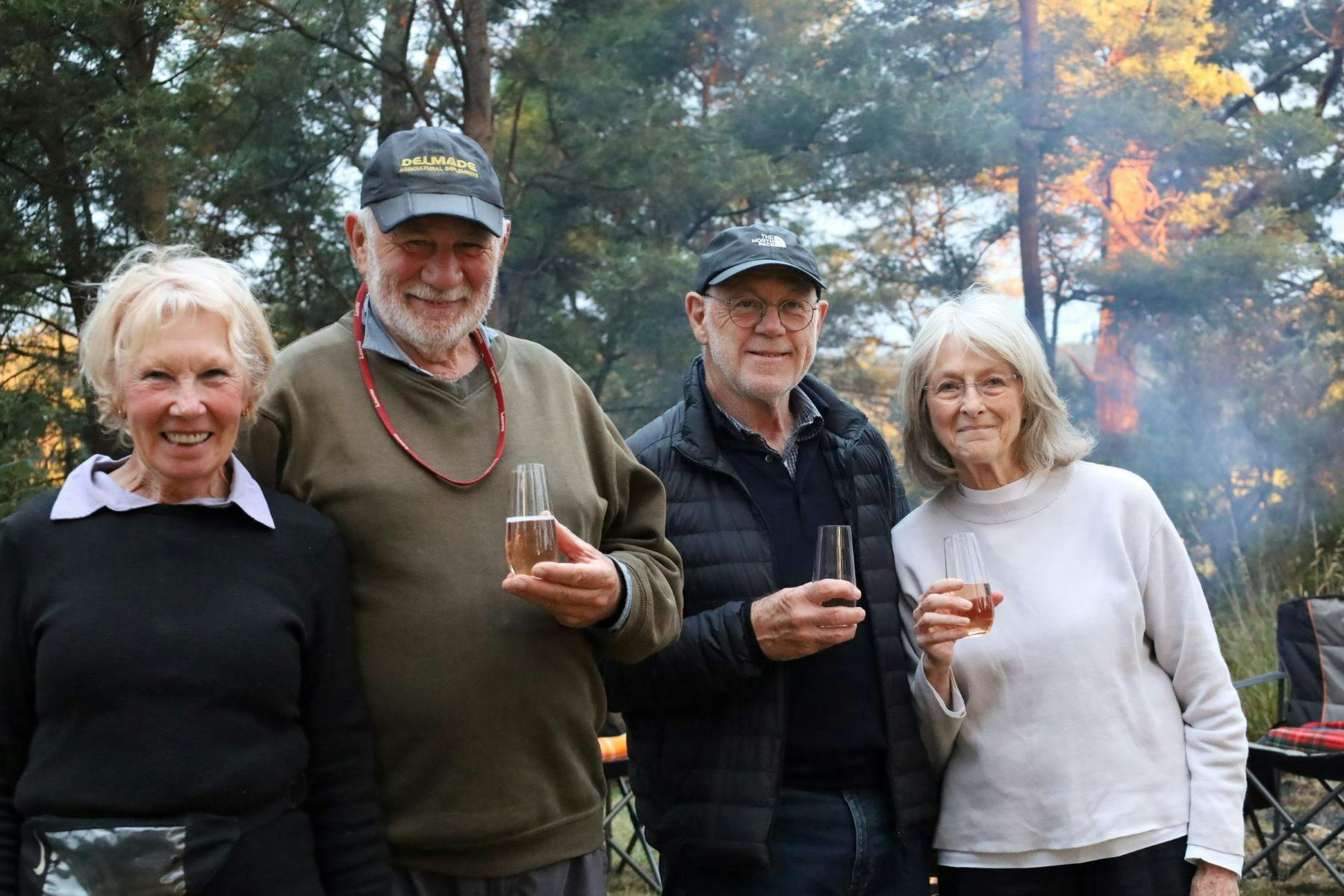 four adults holding a glass of wine with bushland in background