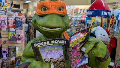 A Ninja Turtle reads a comic book in Impact Comics store