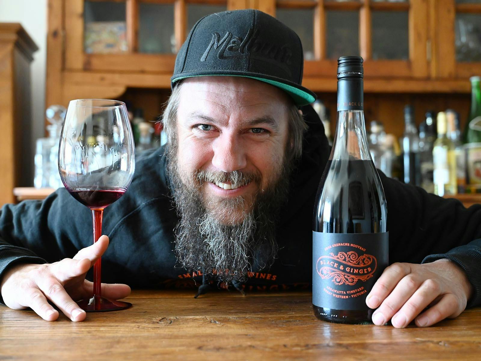 Hadyn Black grinning with a bottle and glass of Grenache in hand