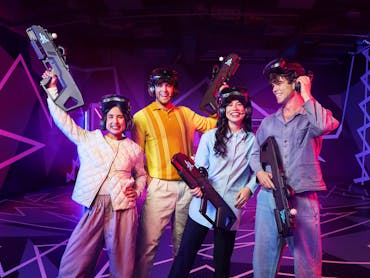 A group of four peolpe pose victoriously in the arena. They look directly to the camera, smiling. A group of four peolpe pose victoriously in the arena. They look directly to the camera, smiling.