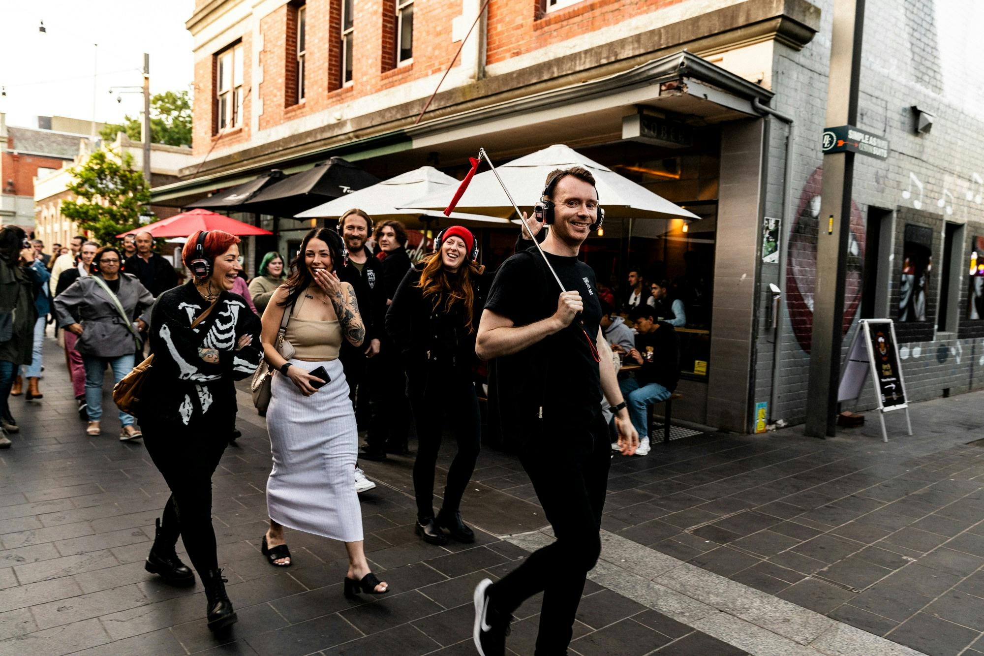 Man in a black t-shirt holding a red flag leading a tour of laughing people down a street