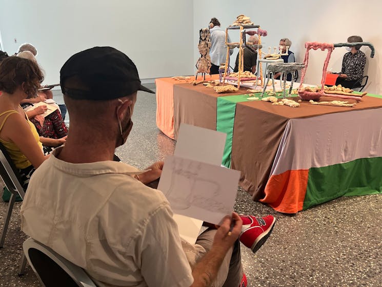 Man in foreground with many participants in circle around an art installation, with sketchbooks