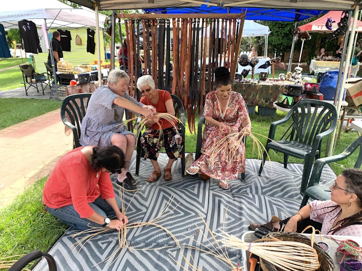 Four ladies weaving a part made basket and getting help.