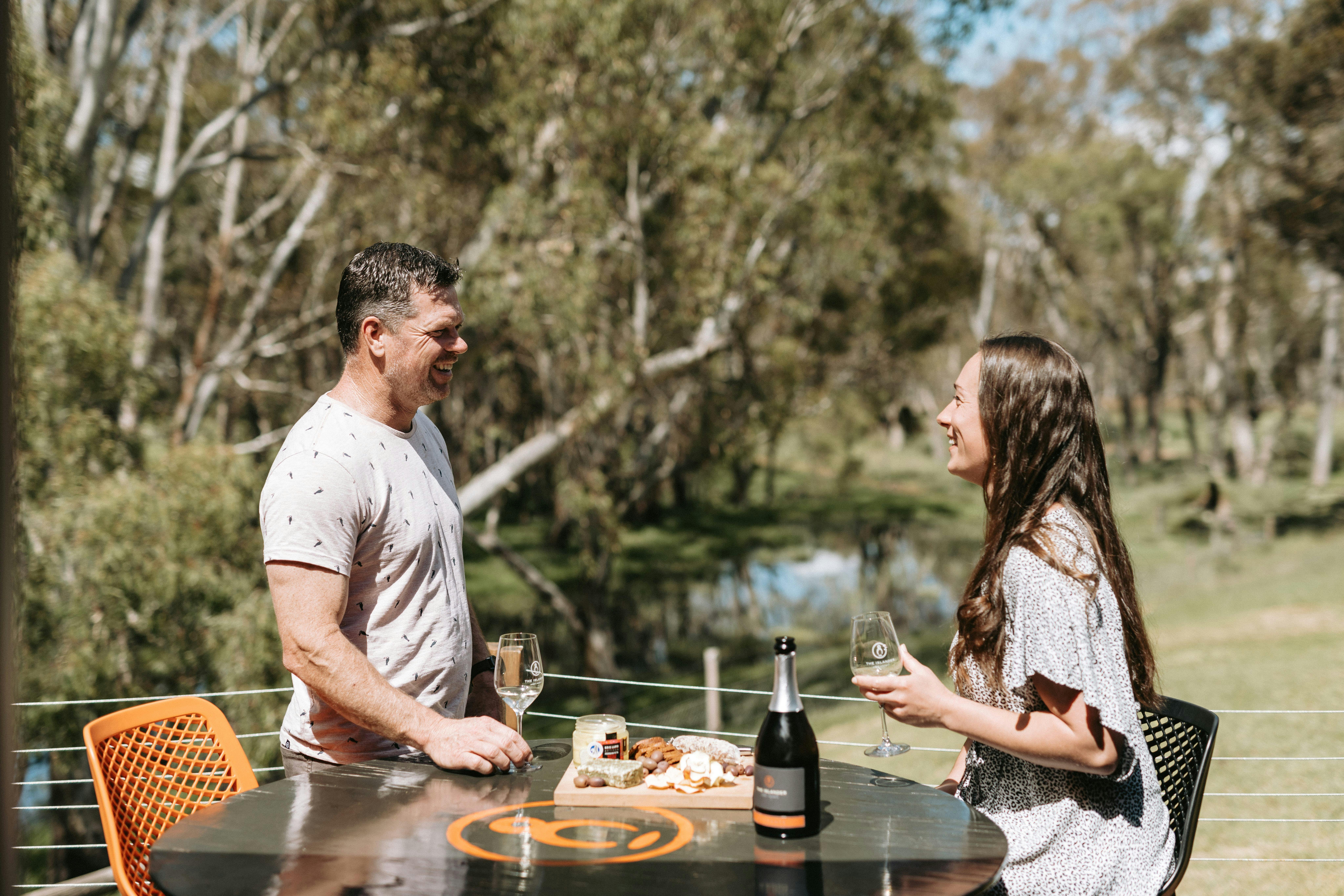 Couple enjoying a glass of wine and a platter on the deck of The Islander Estate Tasting Room