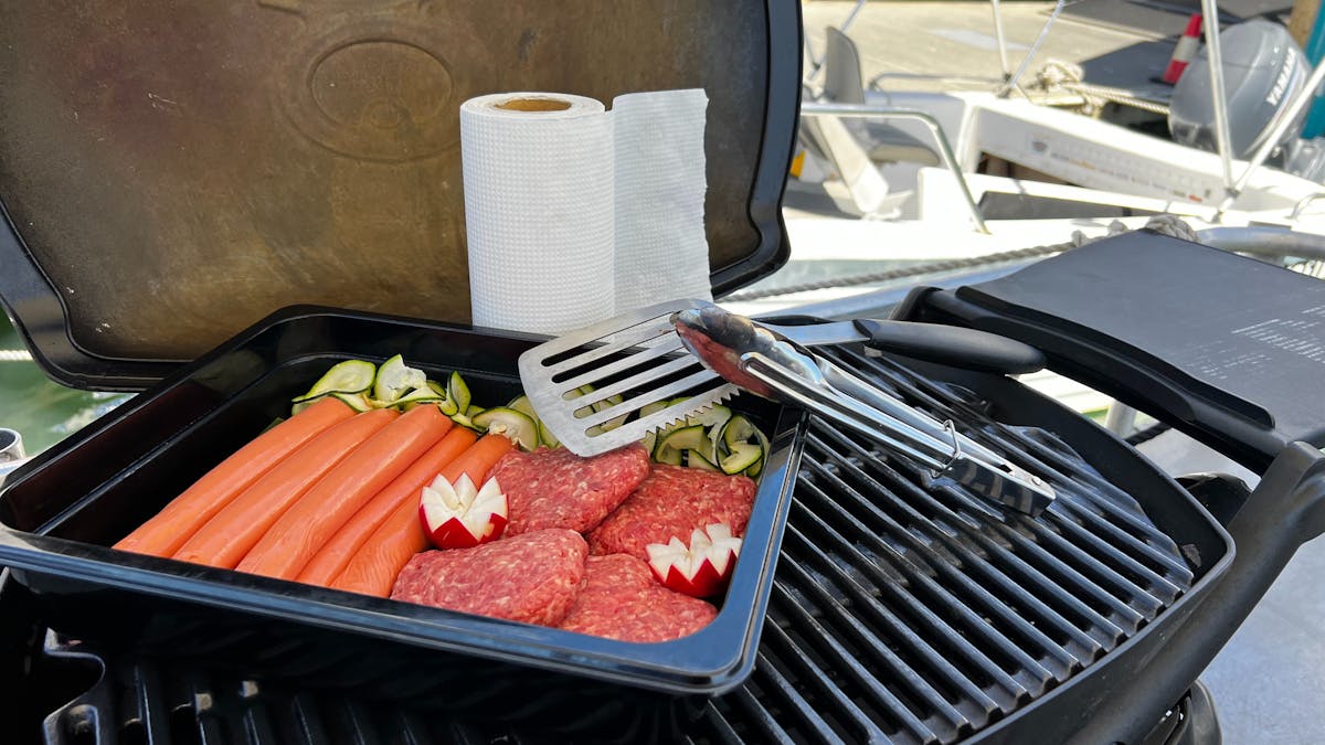 Platter of sausages and patties on a hire BBQ with utensils available with Cairns Boat Hire Booking
