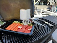 Platter of sausages and patties on a hire BBQ with utensils available with Cairns Boat Hire Booking