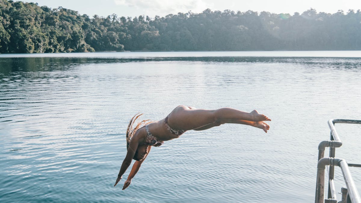 A woman in an arch dive into the crater Lake Eacham from a dock in Tropical North Queensland