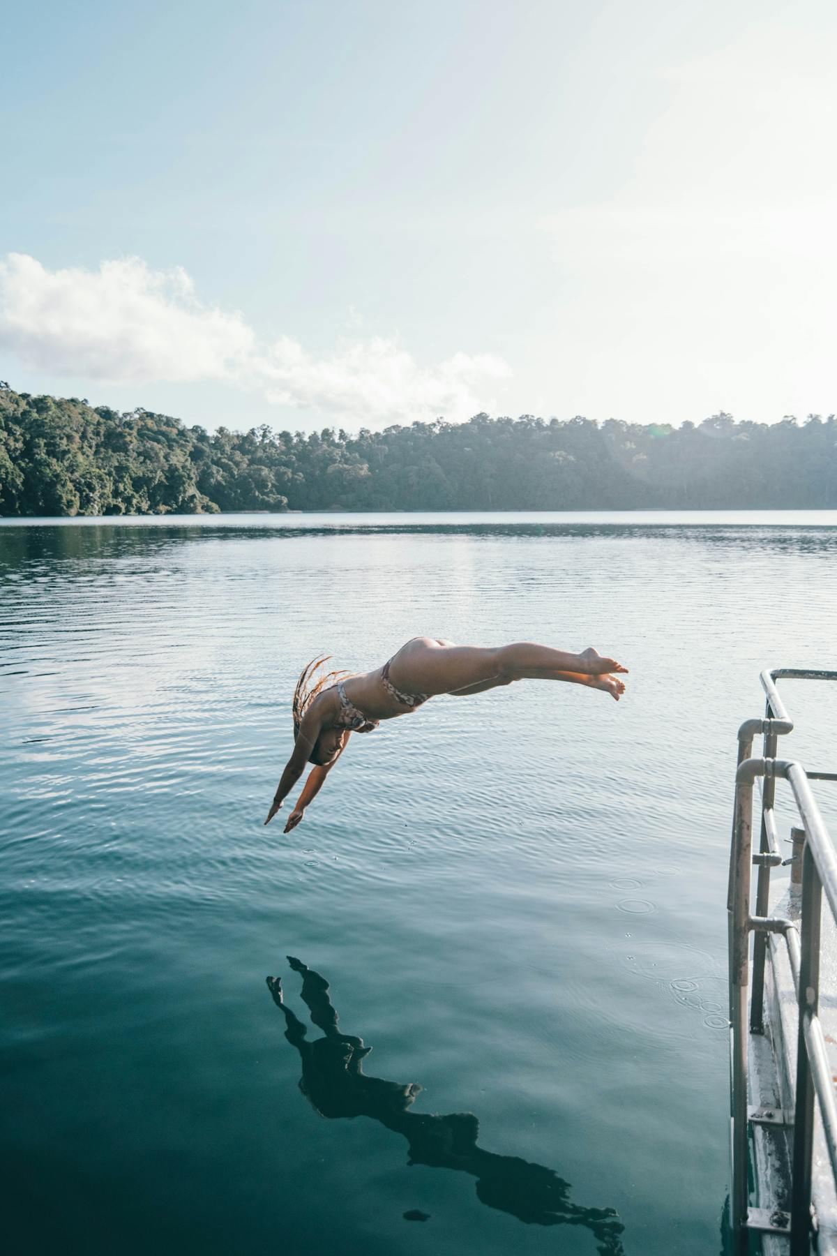A woman in an arch dive into the crater Lake Eacham from a dock in Tropical North Queensland