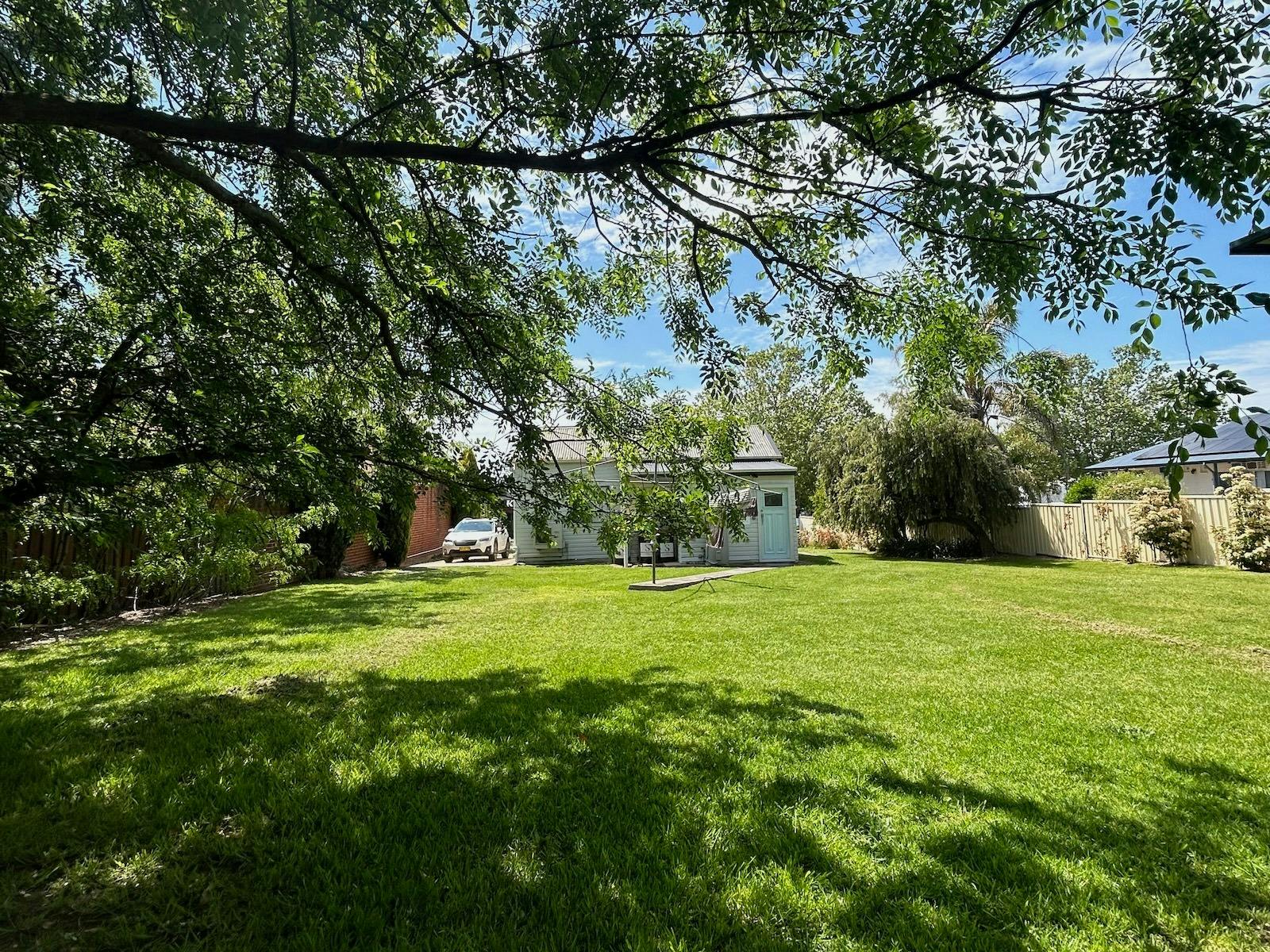 A spacious backyard with lush green grass, shaded by tree branches, and a small cottage in view.