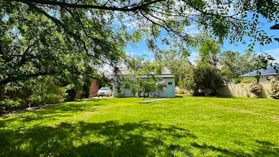 A spacious backyard with lush green grass, shaded by tree branches, and a small cottage in view.