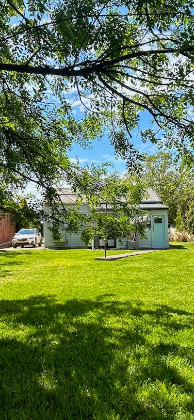 A spacious backyard with lush green grass, shaded by tree branches, and a small cottage in view.