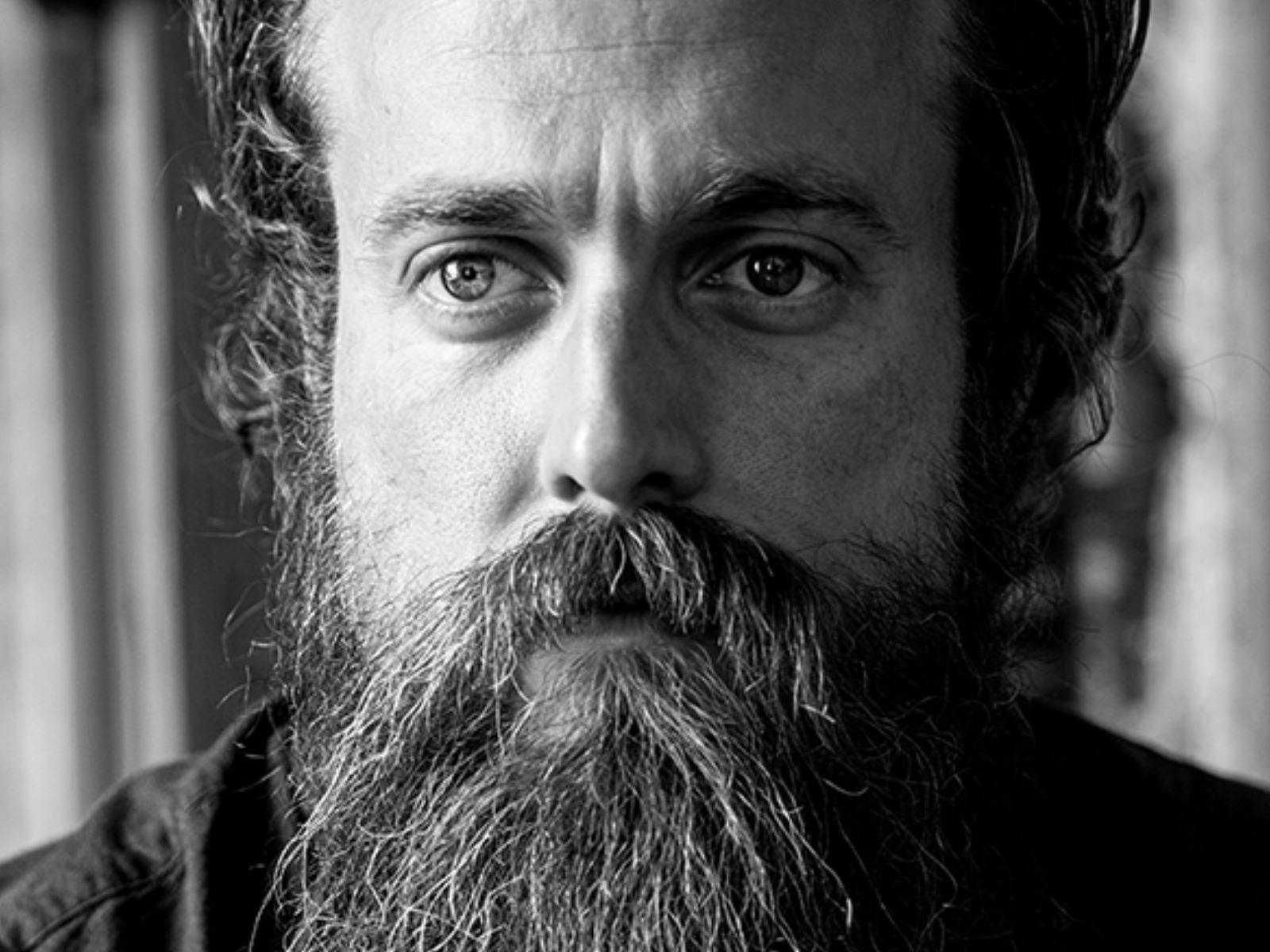 Black-and-white close-up portrait of a bearded man looking directly at the camera.