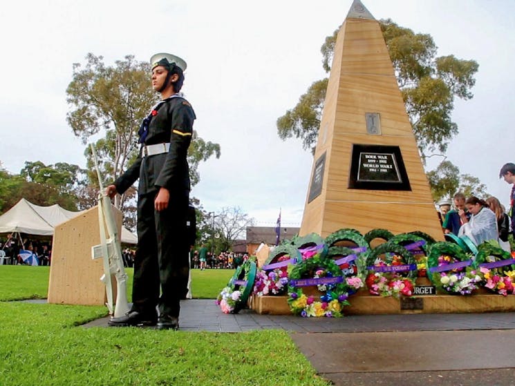 Anzac Day commemoration with soldier standing next to flowers and a grave