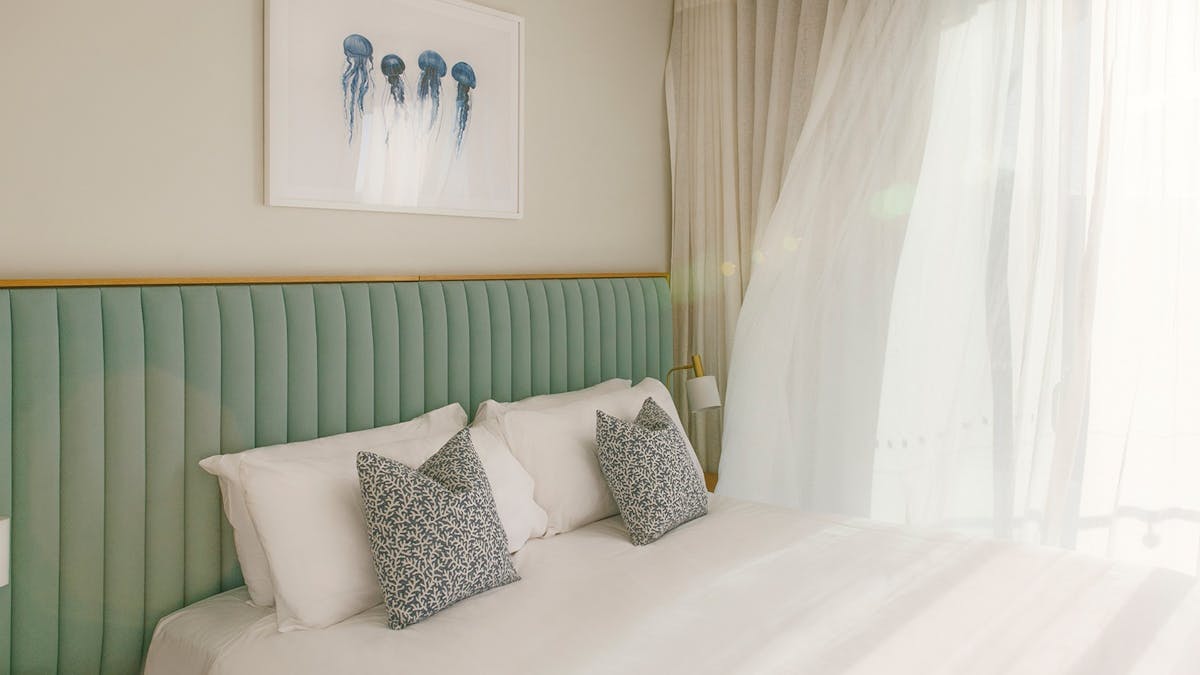 Bright Kirra Point bedroom with king bed, coastal artwork, and sheer curtains flowing in light.