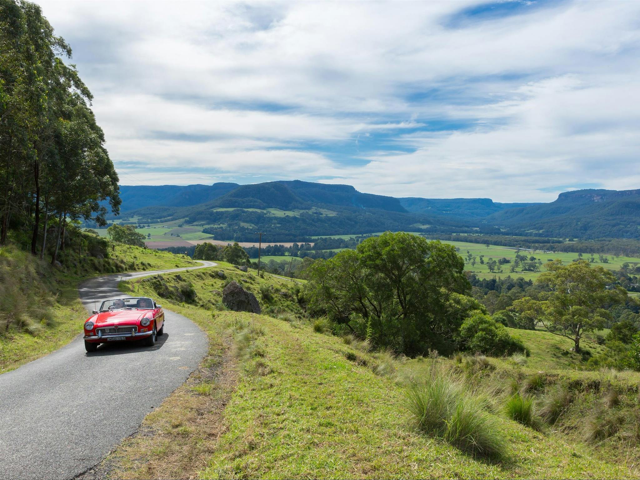 Red car driving along countryside with pretty mountains in the background