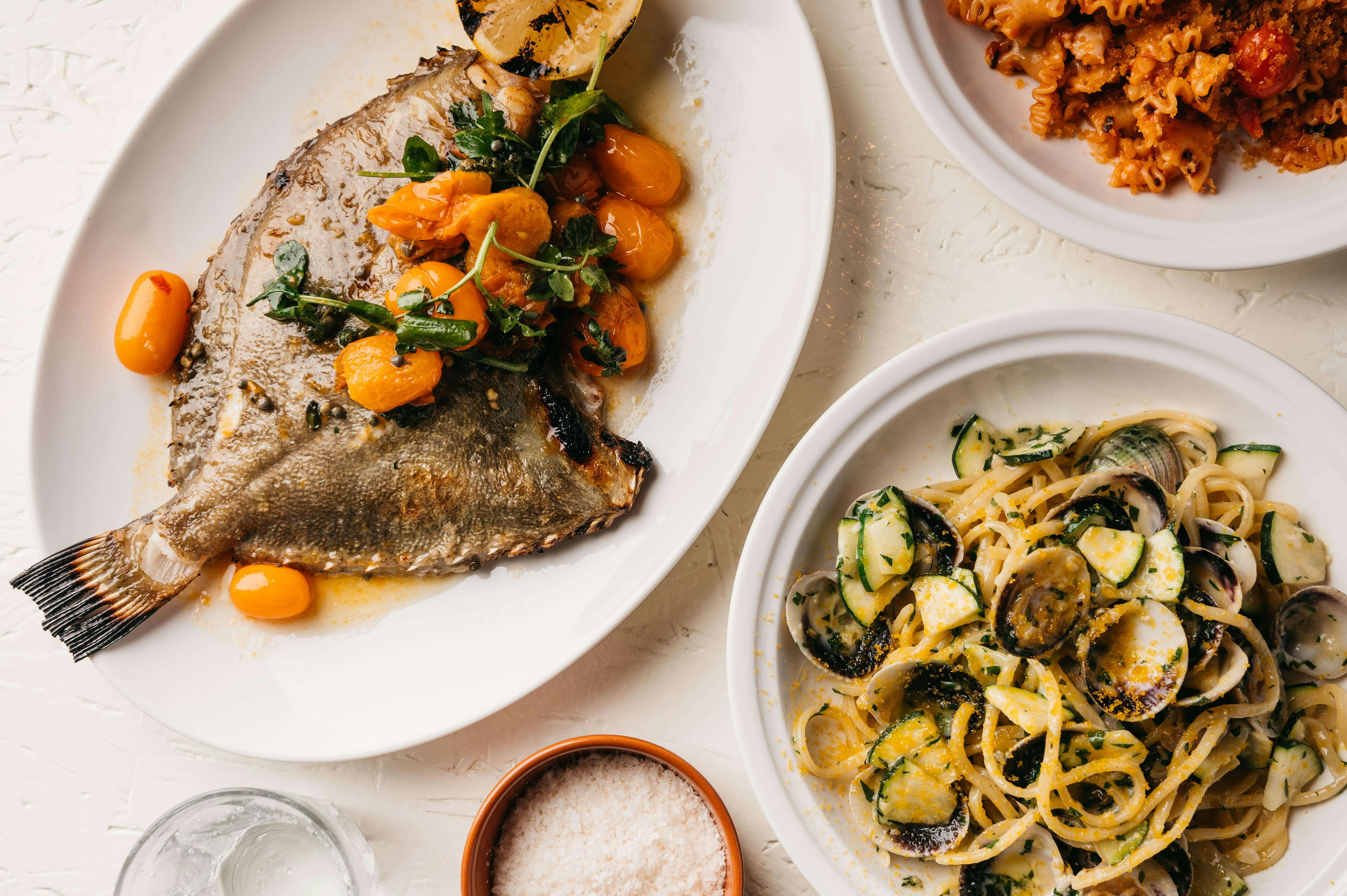Whole fish dish with cherry tomatoes and a seafood pasta dish