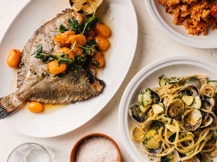 Whole fish dish with cherry tomatoes and a seafood pasta dish