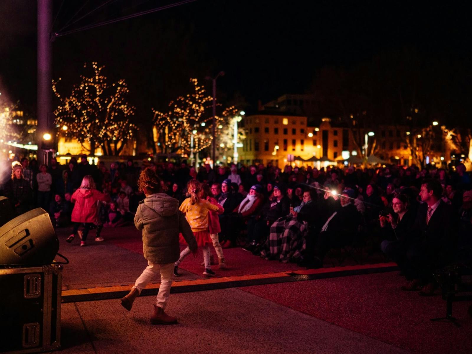 A colour photograph of a seated crowd of people and some children dancing while enjoying live music