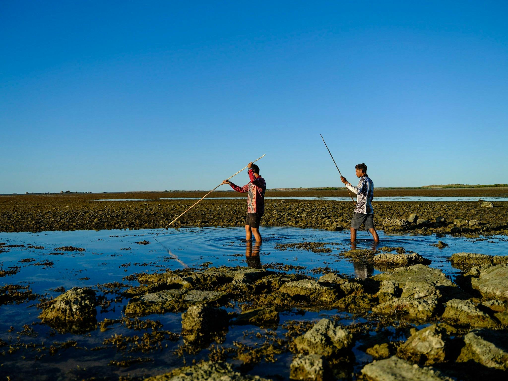 Two boys fishing with spears.