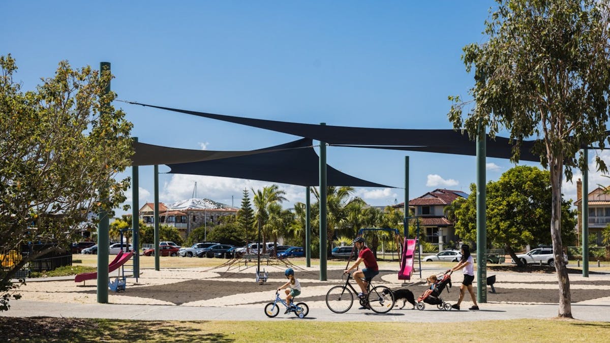 Family cycling together near a playground on a sunny day at Raby Bay Foreshore, Redlands Coast, QLD