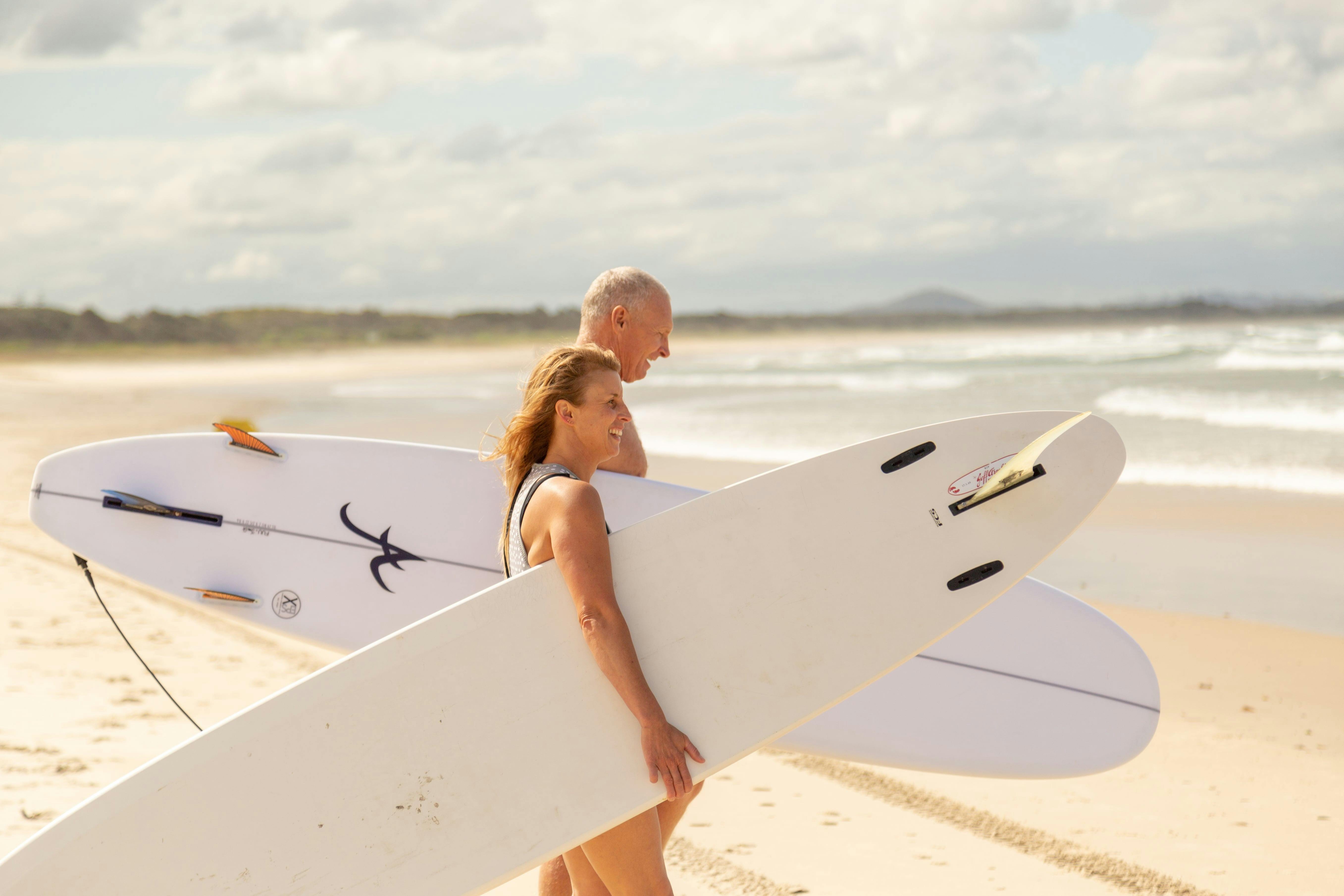 Lady and a man walking their surfboard down the beach