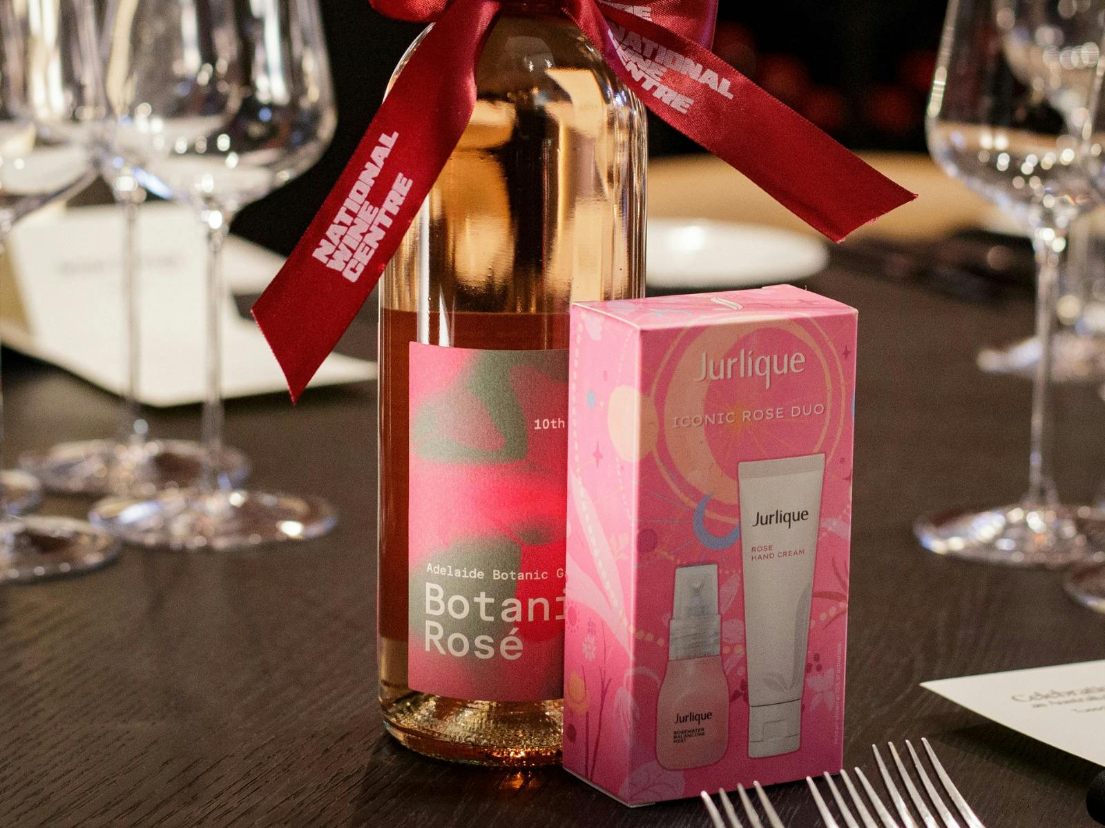 A Botanic Rosé wine bottle stands beside a pink Jurlique rose skincare pack