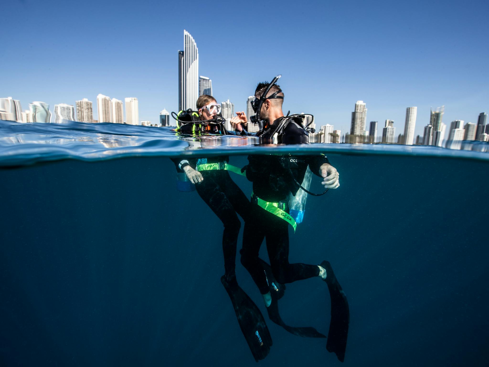 two scuba divers with the Gold Coast city building skyline behind them two scuba divers with the Gold Coast city building skyline behind them