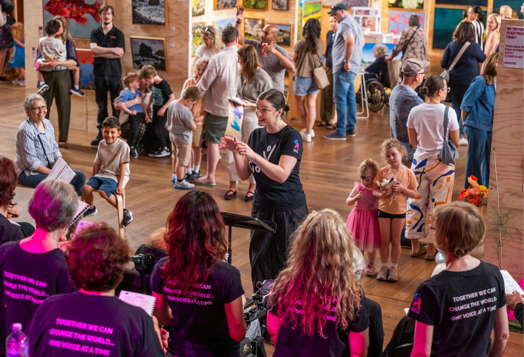 a community choir singing at the art fair with people gathered around enjoying the art and talking.