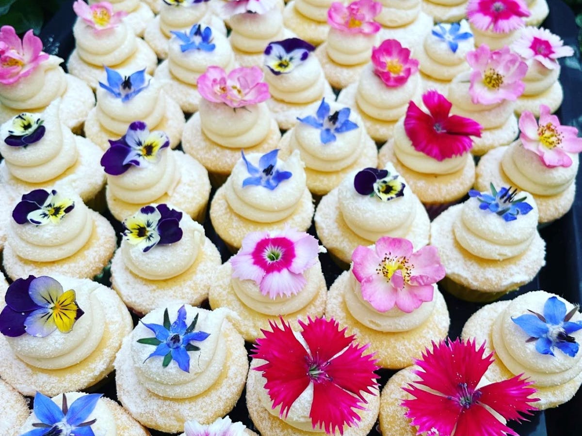 A tray of mini vanilla cupcakes topped with a swirl of icing and colourful edible flowers