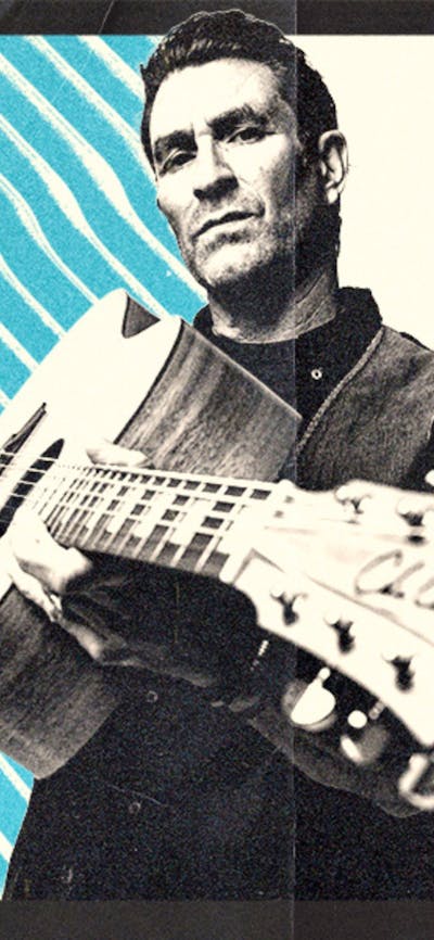A man standing with a guitar facing the camera, with a blue and white background