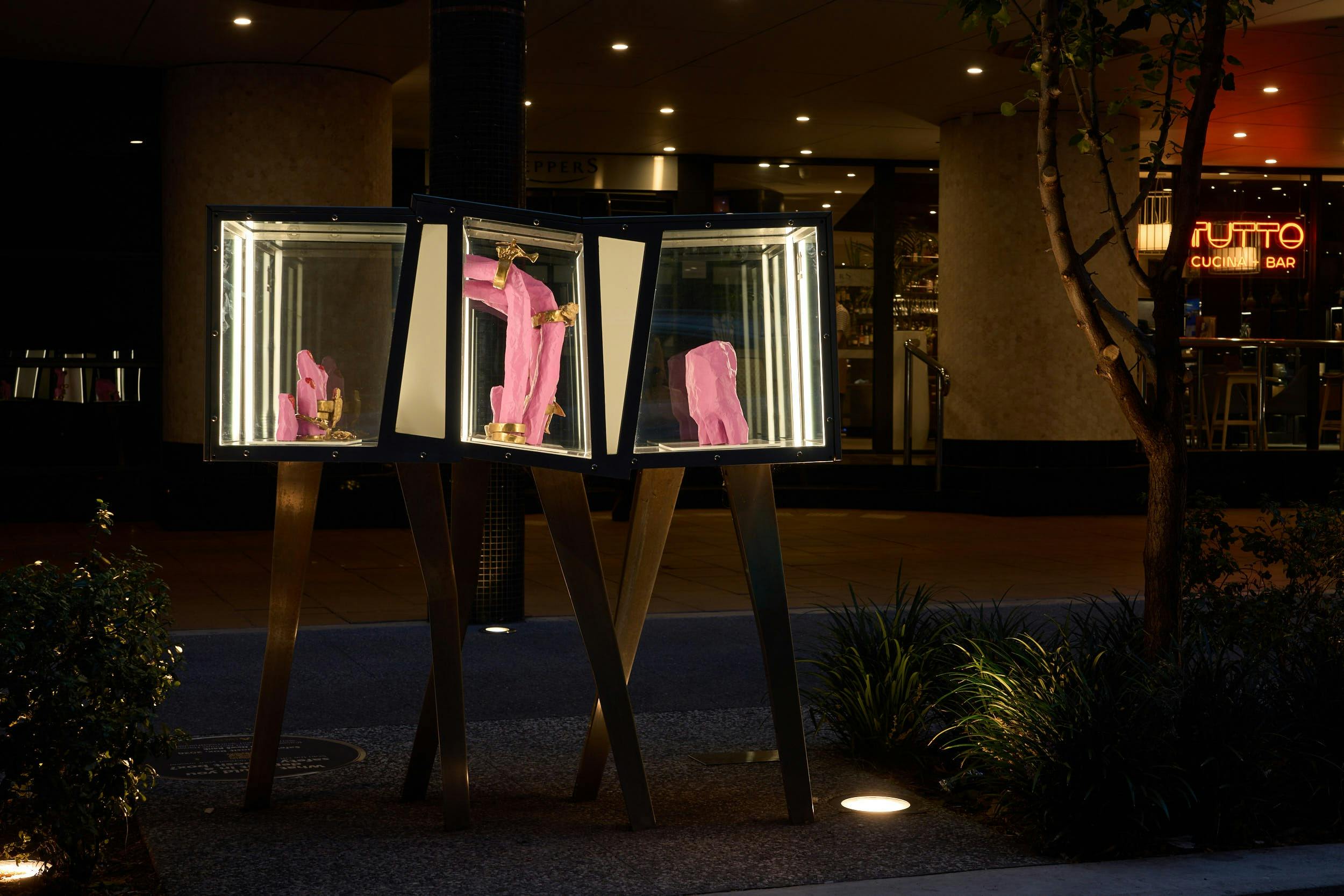 A pink hand covered in golden rings weaves through a transparent box lit from within.
