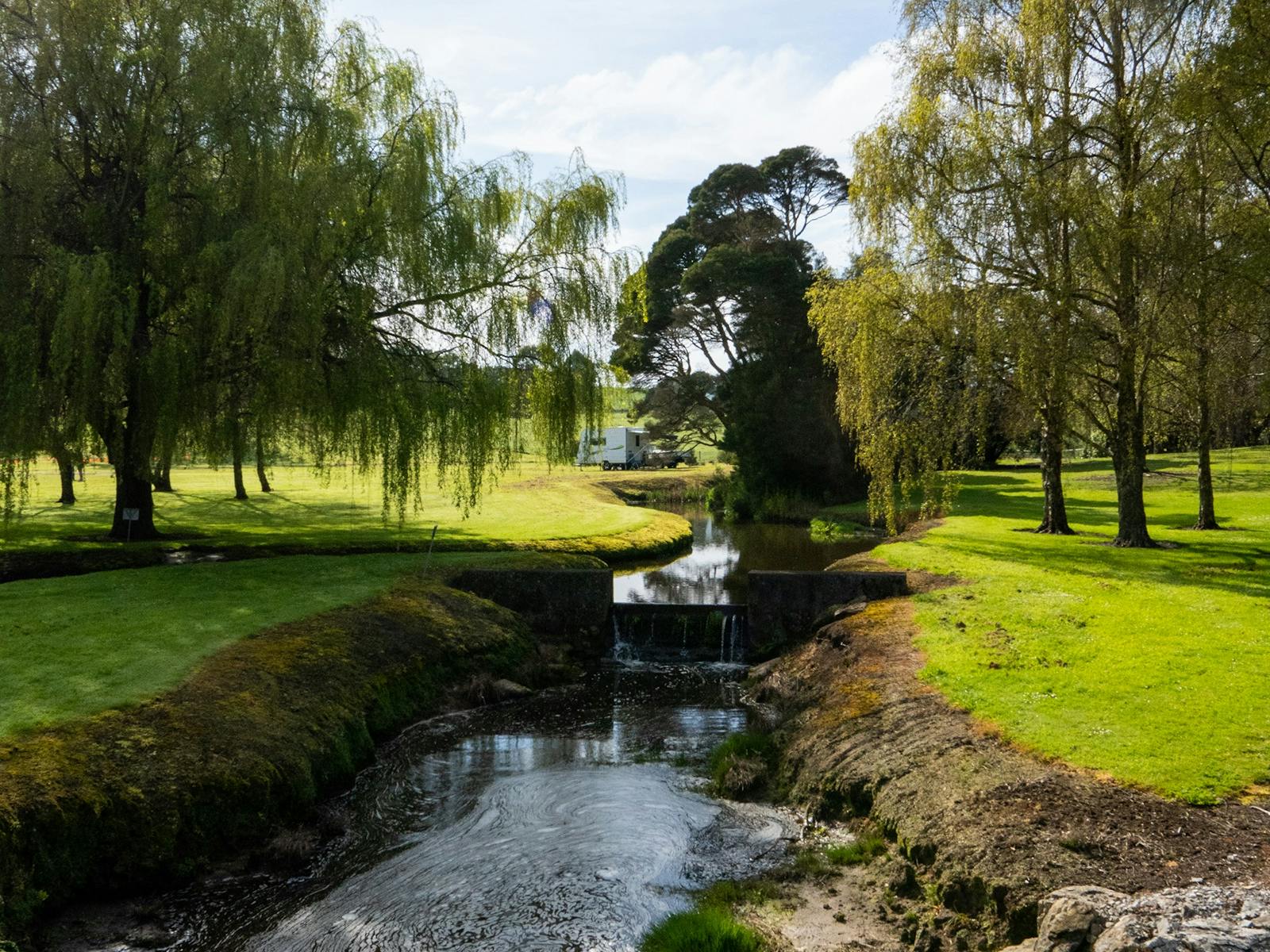 Stream with man-made level change (waterfall effect) framed on each side by trees and vibrant grass