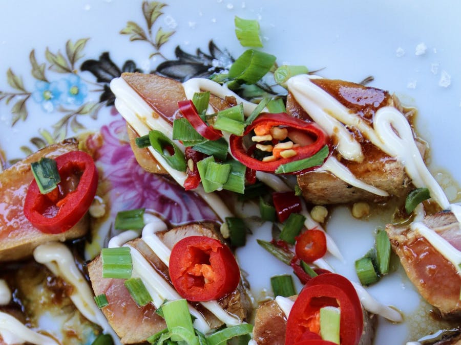 Plate of cooked chicken pieces covered in chilli, shallots, onion and sace